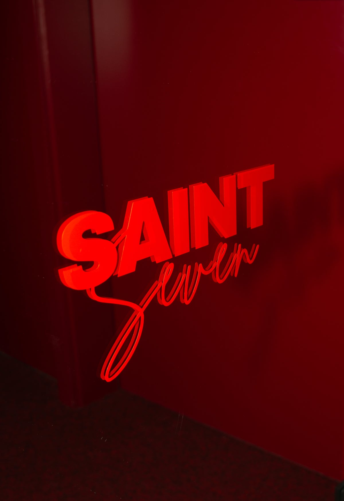 Leuchtender SAINT-SEVEN-Schriftzug in Rot an dunkelroter Wand
